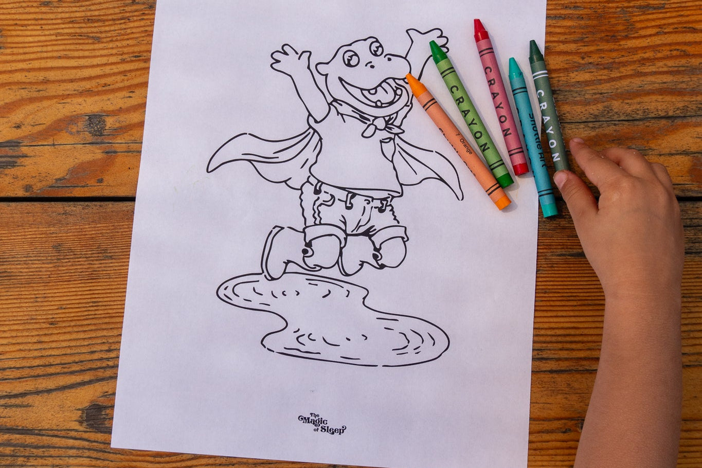 Child coloring a superhero character with crayons on a wooden table