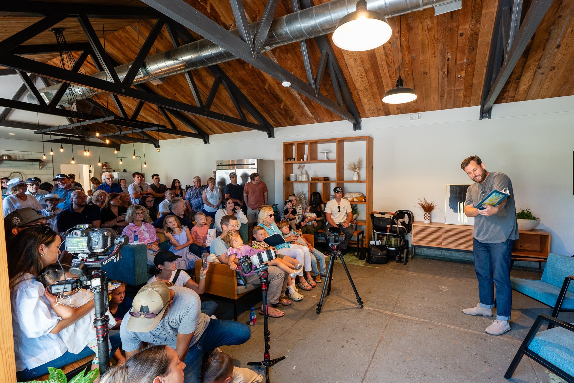 Person giving a presentation in a room with a wooden ceiling and seated audience.