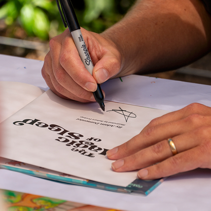 Person signing a book with a Sharpie marker, surrounded by greenery.