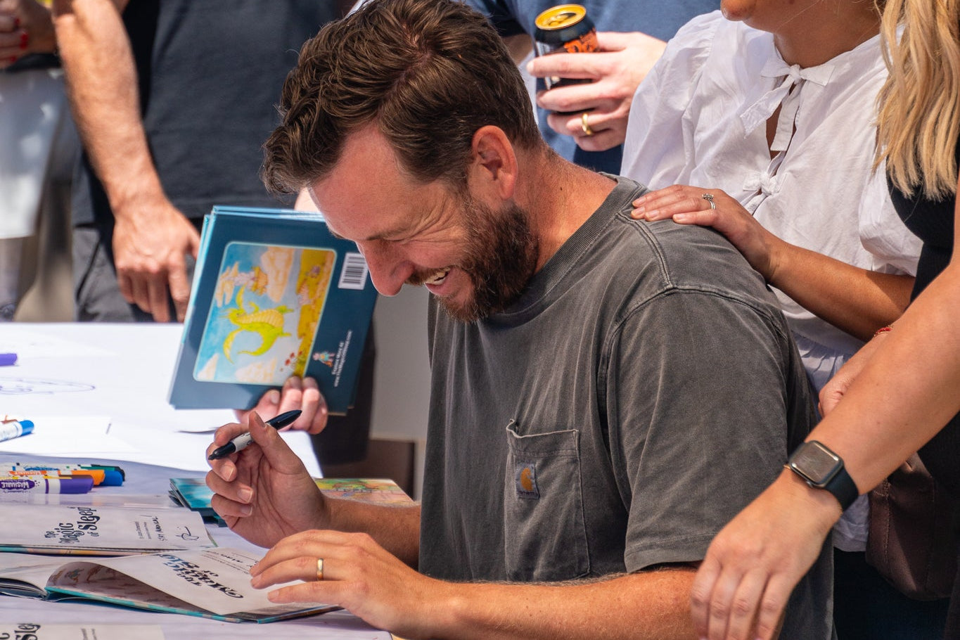 Group of people gathered around a table with a man looking at a tablet device.
